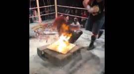 Professional wrestler CHOKESLAMS opponent onto FLAMING board onto of CINDERBLOCKS!