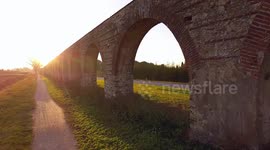Aerial shot, foggy fields, an ancient roman aqueduct in Italy and cars driving behind it, filmed with drone, 4K