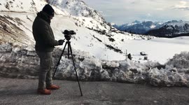 A photographer in high snowy Alps mountains shooting a landscape with a very strong wind, in Italy, 4K