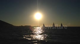 Three yachts sailing with the sunset and Cape Town stadium behind them