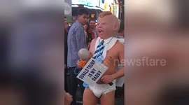 Grown man in diaper and baby face mask holds Trump placard and dances in Times Square