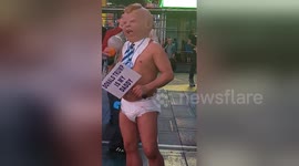Grown man wearing nappy dances on street with hyperrealistic baby face mask