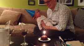 Baby sneezes at candle on birthday cake