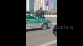 Man sits on bonnet of a taxi driving on road