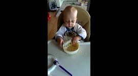 Cute little baby trying to eat with a spoon for the first time