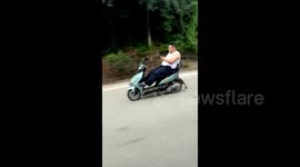 Man drives scooter without holding handle bars while playing on his phone