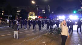 Woman filming herself on cellphone with riot police in background during G20 protest