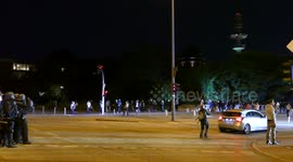 Riot police shining light on people in the street while large police truck advance