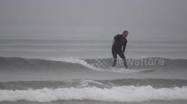 Surfer battles heavy rainfall at Benone beach, Northern Ireland