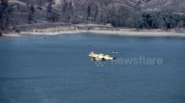 Super scooper aircraft flying low over lake and boats
