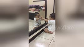 Cute baby plays with 'friend' reflected in mirror
