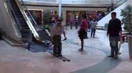 Man in Santa Claus hat descends shopping mall escalator on skis