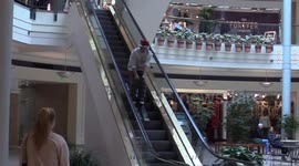 Man in Santa Claus hat descends shopping mall escalator on skis