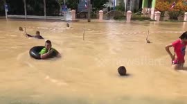 Thai children play on lilos and rubber rings on flooded highway