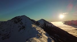 Drone footage at sunrise of temperature inversion with clouds below mountain peak