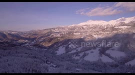 Aerial, beautiful woods under the snow and the view on the snowy mountains with ski tracks