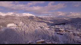 Aerial, beautiful woods under the snow and the view on the snowy mountains with little villages in winter