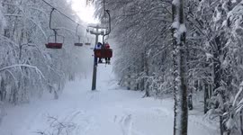 Going up on a chair lift in mountains in the middle of snowy wood