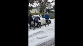 Group of people help push car up snowy hill