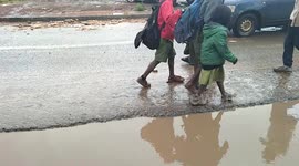 Pupils head home early following heavy rains that submerged their school. One walks bear foot after their shoes are drenched in water.