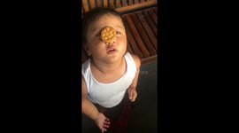 Adorable toddler tries to eat a biscuit balanced on her nose