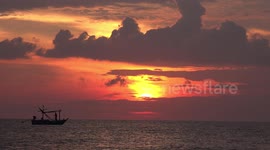 Sunrise over the ocean, with orange sky and fishing boat.