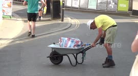 Old hunchback man struggles with wheel barrow in heat wave