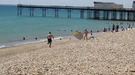 Man chases his beach parasol as it is blown away by a gust of wind