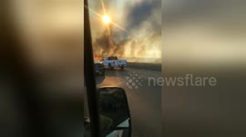 Vehicles drive along California freeway as fast-moving brush fire burns on both sides