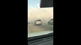 Cars move slowly on highway shrouded in smoke as brush fire burns scarily close