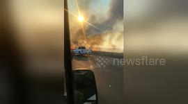 Vehicles drive along California freeway as fast-moving brush fire burns on both sides