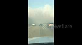 Cars move slowly on highway shrouded in smoke as brush fire burns adjacent