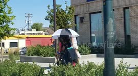 Family avoids sun on a 100-degree day by riding on a motorized wheelchair with an umbrella