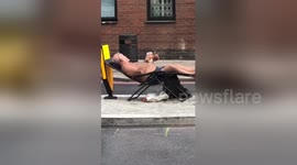 Bare-chested man reclines on chair with drink in middle of London street