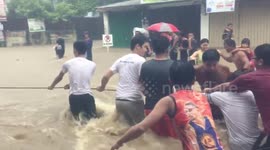 Philippine locals cling to rope to cross street as raging floodwaters form massive current