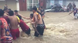 Philippine locals cling to rope to cross street as raging floodwaters form massive current