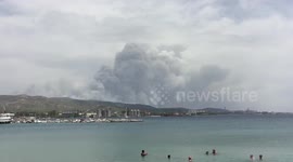 Beach-goers relax in water as smoke from Kineta fire billows in distance