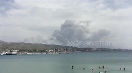 Newsflare Edit - Beach-goers relax in water as smoke from Kineta fire billows in distance
