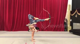 Kid performs impressive archery routine with feet while little girl clings to her
