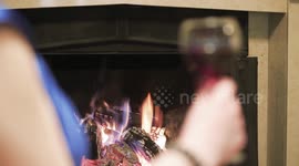 The girl is drinking red wine by the fireplace