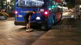 Guy getting a free mall ride on a bus but from the back of the bus holding it and in a skateboard