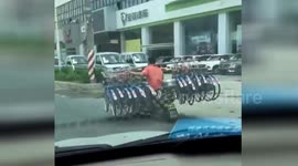 Scooter rider carries 16 bikes on shoulder while driving down road