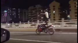 Dangerous rider stands upright on moving motorbike