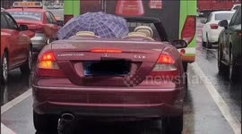 Man holds umbrella while driving convertible in rain