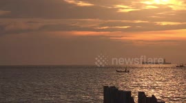 Thai fishing boats sail across an ocean sunset sky.