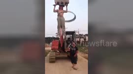 Worker does pull-ups on moving digger while performing hula hoop tricks