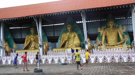 Thai kids play their version of volleyball in front of Buddha statues.