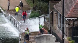 Cyclists wade through cascading water during Lea Bridge Flooding