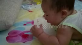 Cute baby tries to eat strawberry pattern on bed sheet