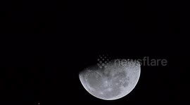 A UFO flies over the moon, casting a shadow as ascends into the heavens.